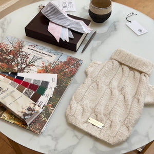 Beige knit hat on a marble coffee table with books and a plant in the background.