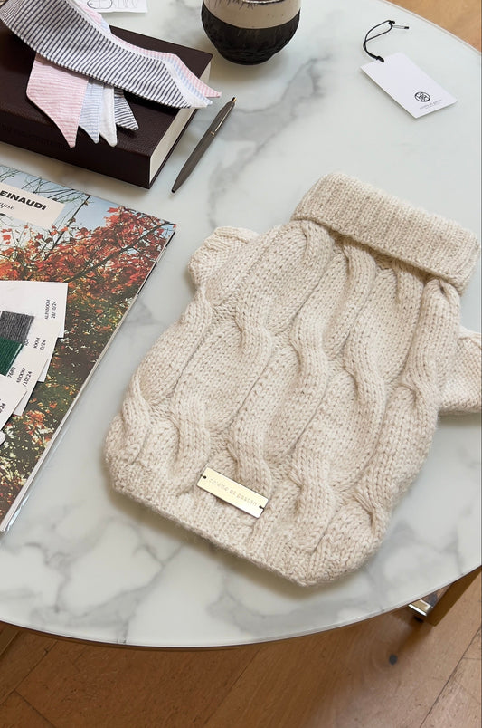Beige knit hat on a marble coffee table with books and a plant in the background.