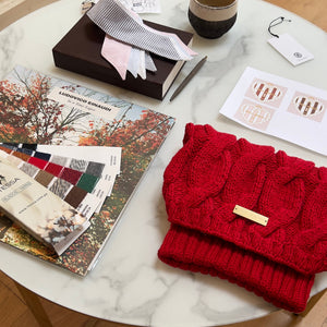 Round marble table with a red knitted bag, books, and a mug on a wooden floor.