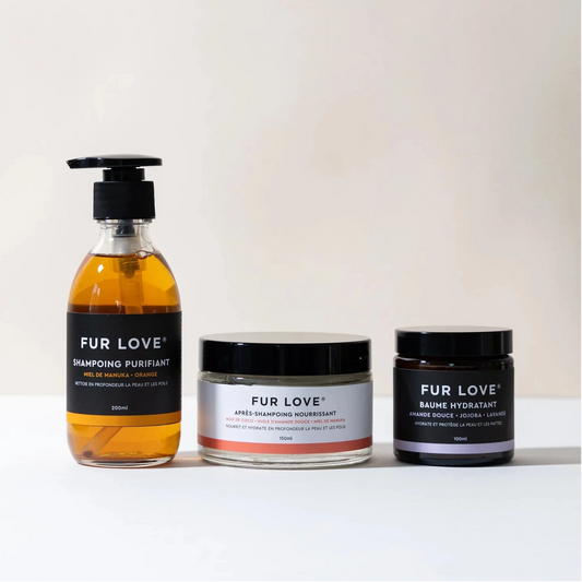 Three Fur Love pet grooming products arranged on a white surface against a light beige background: an amber liquid shampoo bottle with a black pump, a white jar with a black lid, and a dark purple jar with a black lid.